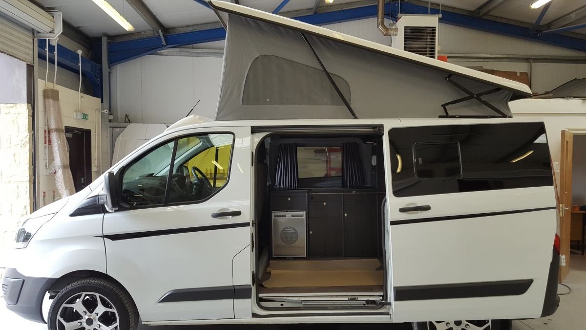 A converted white campervan with an open side door and raised roof