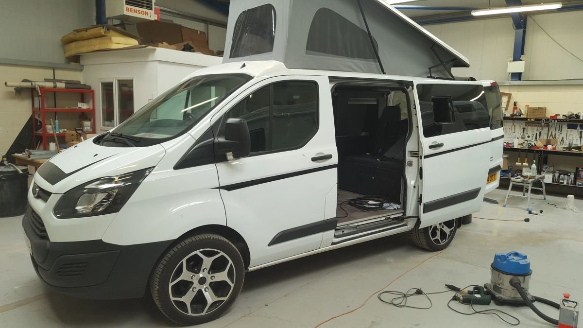 A white campervan with its roof raised in the workshop